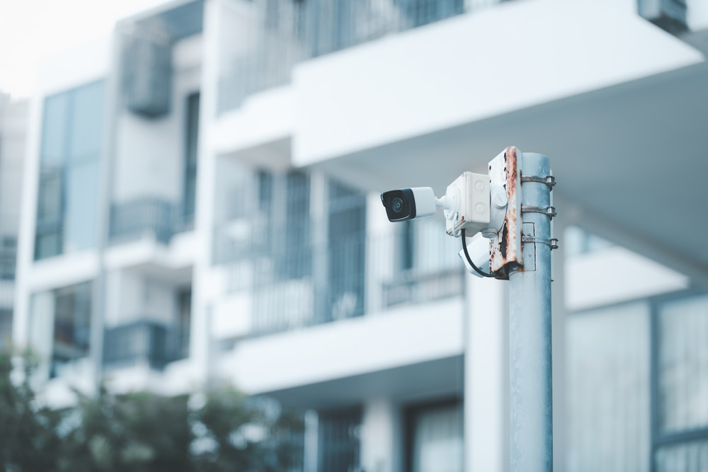 CCTV equipment mounted to post outside white apartment building