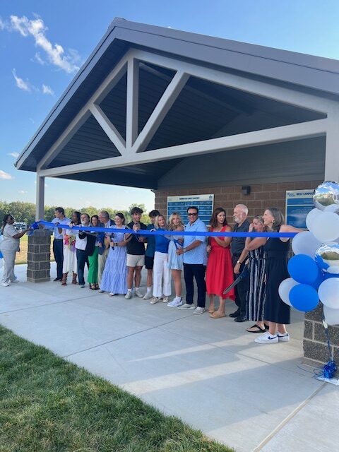 people gathered behind blue ribbon unveiling a new pavilion behind them